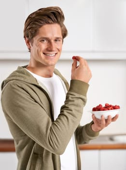 Smile, portrait and man with raspberries in kitchen of home for diet, health and wellness. Happy, confident and male person eating fruit for fresh, organic or nutrition snack in modern apartment.
