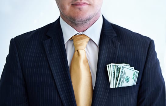 Suit, serious and businessman with money in pocket for bribe, fraud or financial scam in studio. Corruption, pay and closeup of professional male person with cash for crime by white background