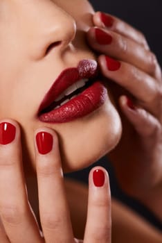 Red, makeup and woman with nail polish and lipstick for cosmetics, hands touching face and cosmetology on black background. Manicure, shine and closeup with bold color, skincare and beauty in studio