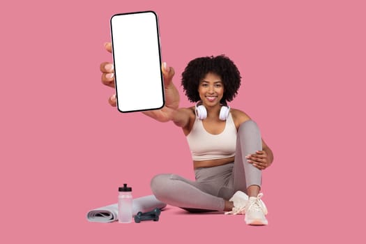 Fit black woman showing phone screen with gym gear