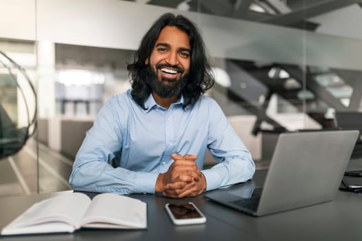 Professional young indian guy sitting at desk with laptop