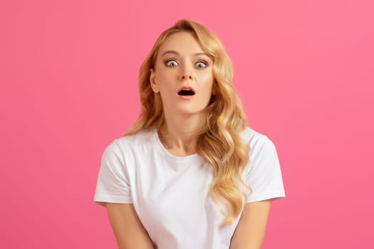 Shocked millennial blonde woman opening her mouth over pink background