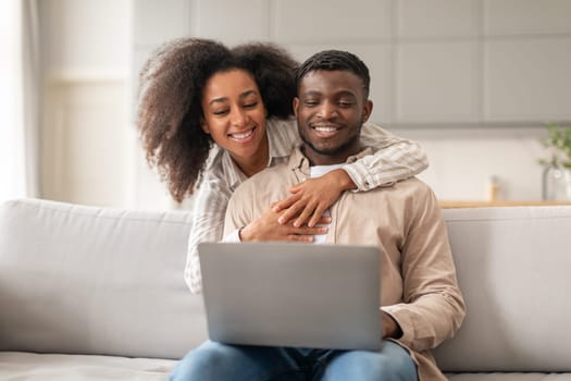 Black couple hugging while using their laptop computer at home