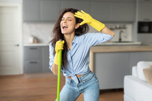 Joyful woman singing with mop like microphone