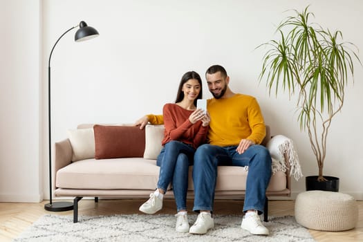 Young Smiling Caucasian Couple Using Mobile Phone And Embracing Together At Home