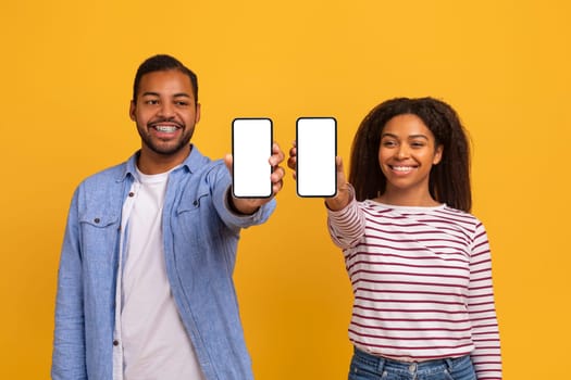 Check This App. Happy black couple showing two smartphones with empty screen