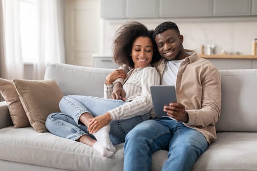 Happy black husband and wife enjoying movie on tablet indoor