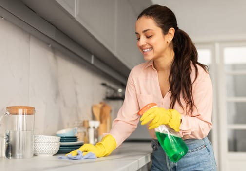 Joyful woman cleaning countertop with spray and cloth