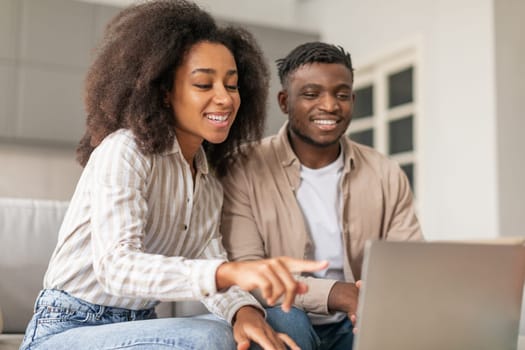 African American couple pointing at screen of laptop at home
