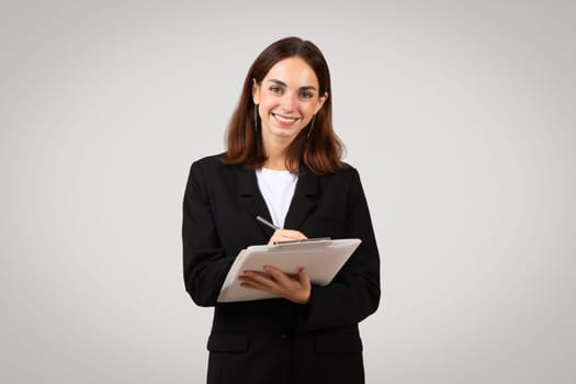 Confident young businesswoman with a warm smile writing on a digital tablet