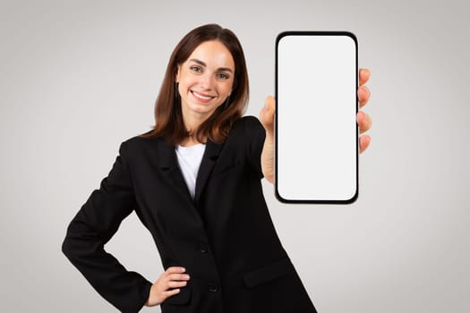Cheerful professional woman presenting a blank smartphone screen, perfect for mockups or ad