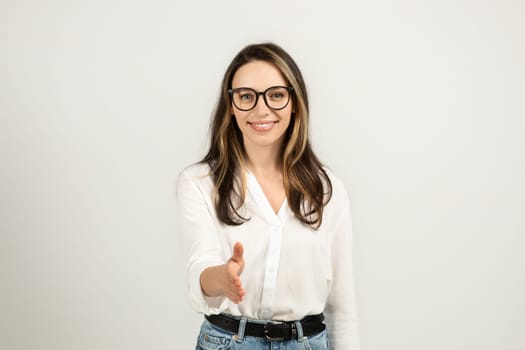 A friendly young woman with long brown hair and glasses extends a handshake while smiling