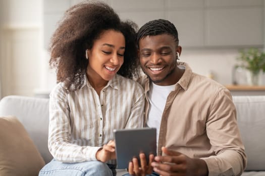 Smiling African couple with wireless earphones using digital tablet indoors