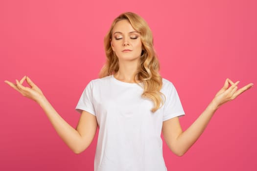blonde young woman in t-shirt with closed eyes meditating, studio