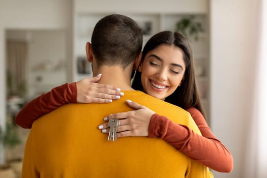Happy young woman hugging husband and holding home keys in hand