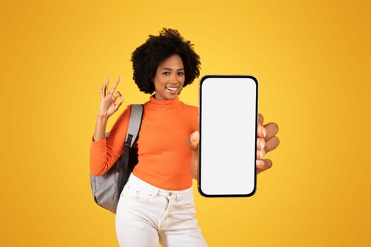 Happy African American woman with afro hair showing OK sign and presenting a smartphone with a blank screen