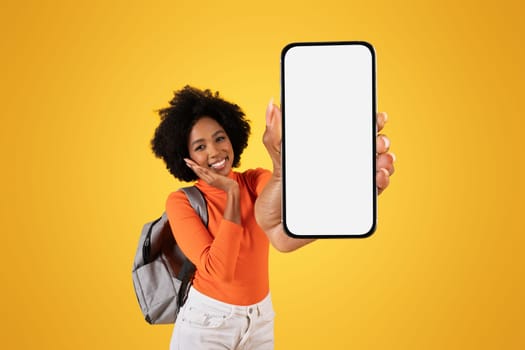 Delighted African American woman with a vibrant afro hairstyle, holding out a phone with a blank screen