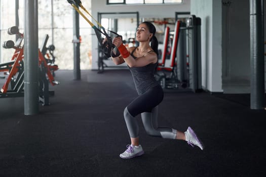 Athlete woman pulling suspension straps in health club
