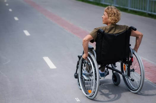 Rear view of an elderly woman in a wheelchair riding on a bike path.