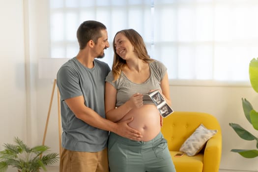 Pregnancy couple hugging looking picture of ultrasound, smiling happily touching belly
