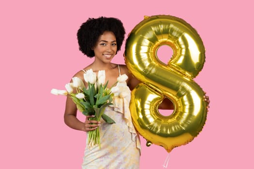 Smiling African American woman with curly hair, holding a bouquet of white tulips and a golden number 8 balloon