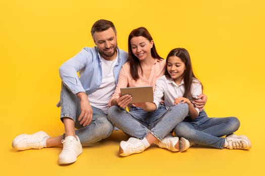 Mom, dad and daughter sitting with digital tablet device, studio