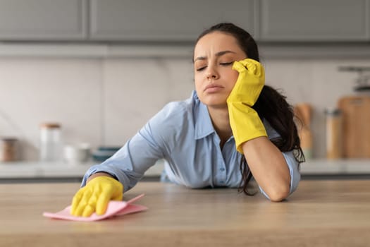 Tired young woman cleaning kitchen countertop