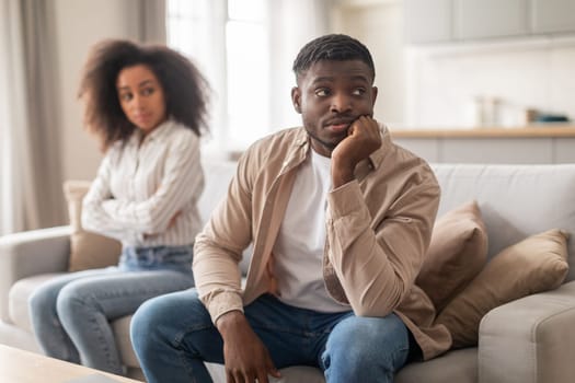 Sulking black boyfriend and offended girlfriend sitting on sofa indoor