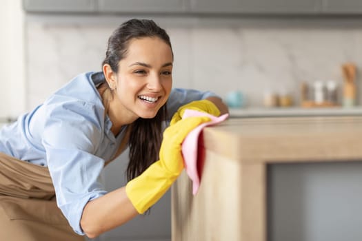 Smiling woman dusting furniture in the kitchen, copy space