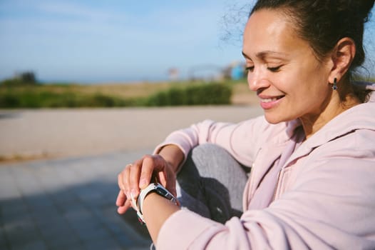 Close-up portrait happy smiling young woman setting up her smartwatch while working out outdoor. People. Fitness. Sport