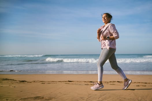 Beautiful woman running on the beach, enjoying outdoor activity, workout on view of Atlantic ocean. Healthy lifestyle.