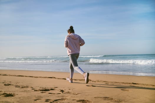 A slim athletic young woman in sportswear running on the Atlantic beach, leaving footsteps in the wet sand