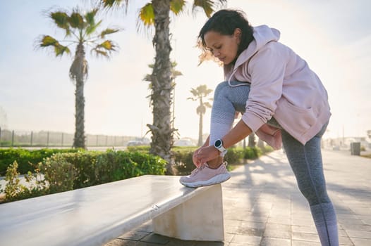 Young athletic woman tying laces on her sports shoes, ready for morning run on the coastal promenade or outdoor workout