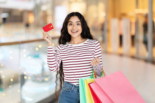 Cheerful woman with credit card, colorful bags at the mall