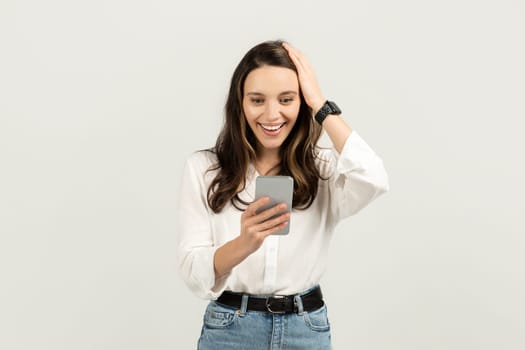 Surprised and delighted woman looking at her smartphone with one hand on her head