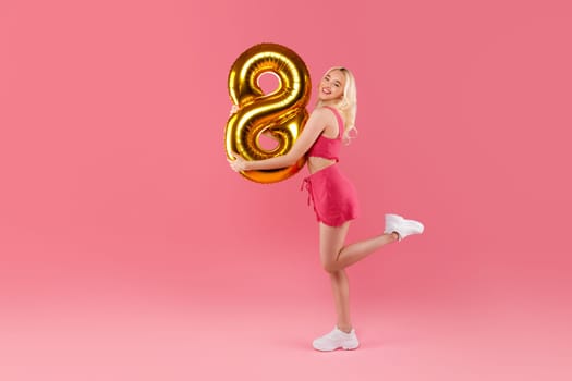 Playful young woman with 8 balloon in pink shorts, full length
