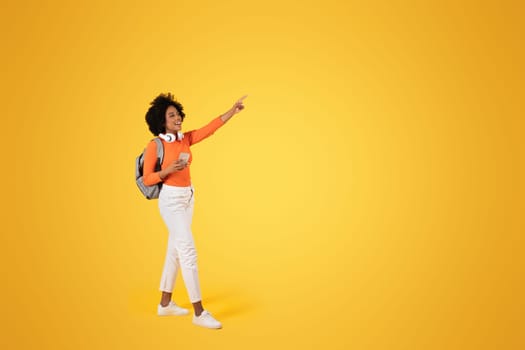 Joyful African American woman with curly hair, pointing with excitement, holding a phone