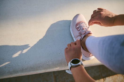 Overhead view sportswoman tying laces on pink sports sneakers, wearing smart wristwatch, ready for morning run, workout