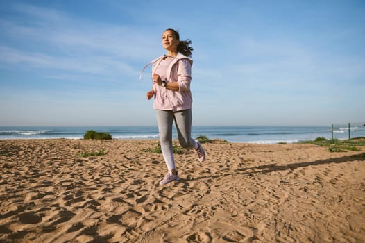 Active determined fit woman burning calories during morning jog on the sandy beach.