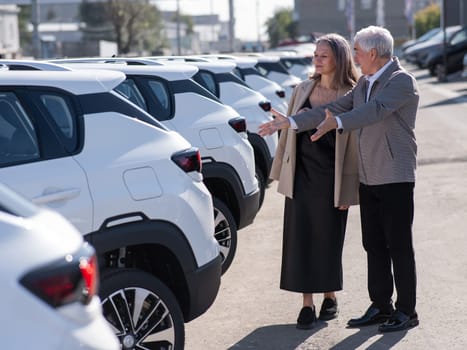 Mature Caucasian couple walks past cars outdoors, choosing a new one.