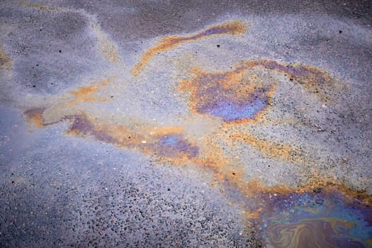 Colorful rainbow stains of an oil spill on wet asphalt