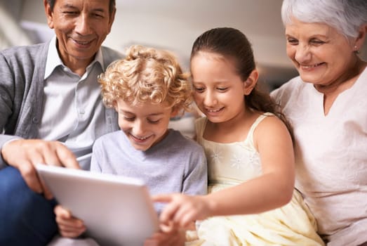 Happy family, grandparents and kids with tablet for entertainment or social media on sofa at home. Grandma, grandpa and children with smile, hug and love on technology for bonding or game at house