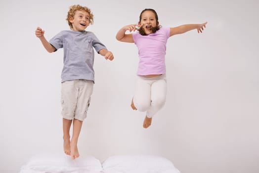 Jumping, bed and kids with fun, energy and morning in a bedroom with game and sibling. Youth, hop and home with a excited children on a duvet in air with crazy play and leap in house with friends