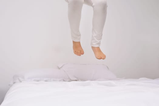 Jumping, bed and kid with fun, energy and morning in a bedroom with game and feet. Youth, hop and home with a excited child on a duvet in air with crazy play, leap and legs in house with white wall