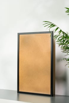 Black wooden photo frame and plant on gray background
