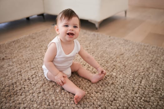 Happy, sweet and baby on carpet playing for child development in living room at house. Smile, cute and adorable young infant, toddler or kid sitting on floor rug for growth in lounge of modern home
