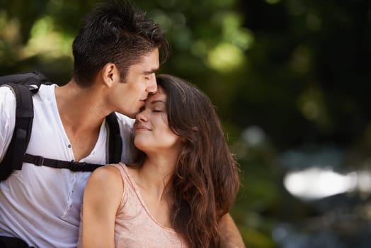 Kiss, nature and couple in forest for hiking, trekking and adventure for wellness, relax and explore. Dating, love and man and woman on holiday, vacation and travel on weekend for bonding outdoors