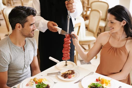Couple, restaurant and waiter serving food or sausage kebab on skewer for fine dining, anniversary or nutrition. Man, woman and relationship bonding dates in Italy with water carving, meal or eating