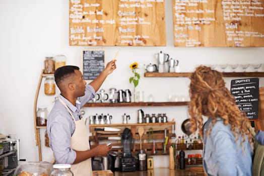 Coffee shop, customer and barista with pointing at menu for purchase, decision and service at restaurant. Waiter, small business and woman at cafe with options, discussion and choice for lunch order