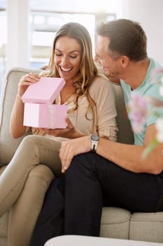 Happy woman, surprise and open gift of man in lounge, excited and couple to celebrate valentines day in home. Husband, love and present for wife with kindness, gratitude and wow together on weekend
